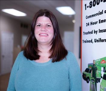 A lady with medium length dark brown hair, brown eyes and a blue shirt in front of a SERVPRO sign
